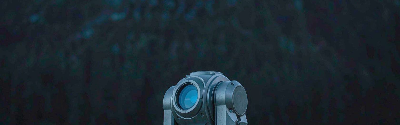 Close-up of a terrestrial laser scanner head on its tripod, standing on open hillside at blue hour.